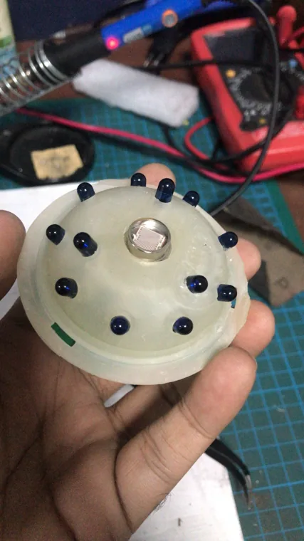 Hand holding a circular translucent assembly with components around its edge.