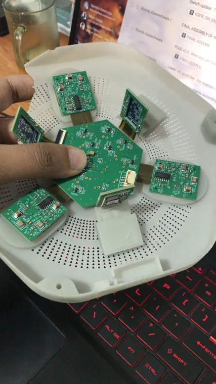 Hand holding a circular PCB over a disassembled white device enclosure.