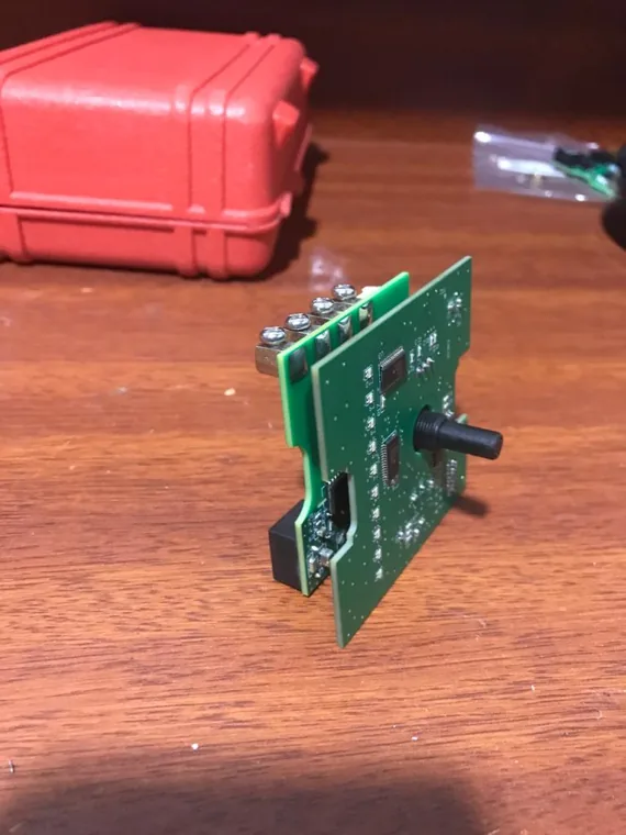 Upright green PCB with a black rotary control shaft on a desk.